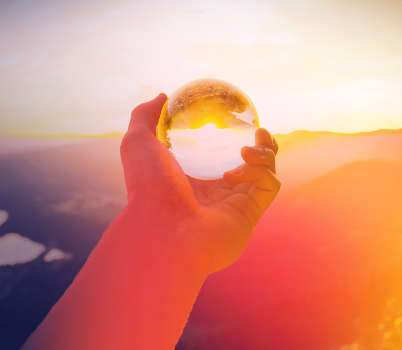 stylized photo of hand holding a crystal ball over looking sunset, original photo by Arthur Ogleznev